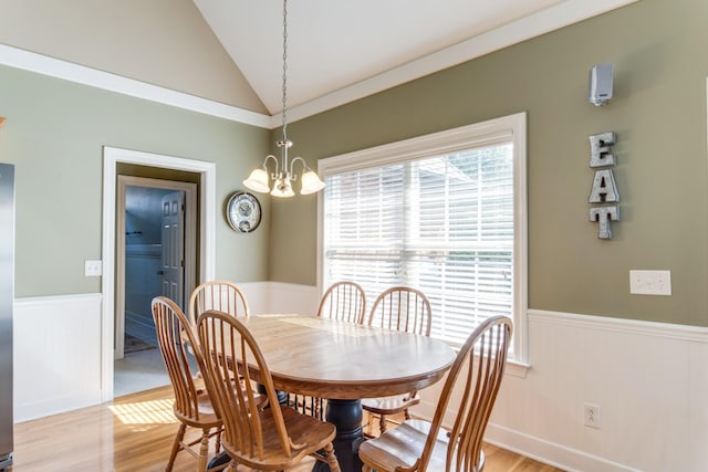 dining space with a wainscoted wall, lofted ceiling, and light wood-style floors