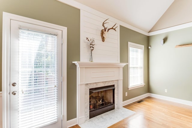 unfurnished living room with vaulted ceiling, baseboards, a high end fireplace, and light wood-style floors