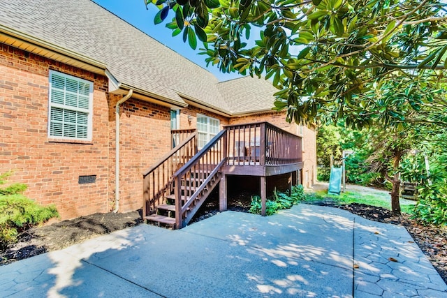 rear view of property with crawl space, roof with shingles, brick siding, and a patio