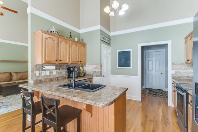 kitchen featuring a peninsula, a breakfast bar, a towering ceiling, stainless steel electric range oven, and light wood finished floors