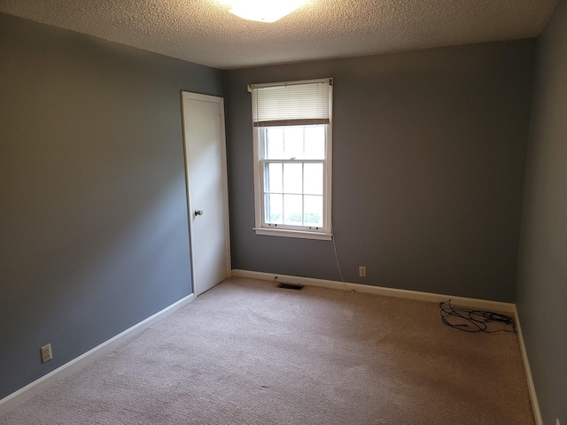 spare room featuring baseboards, visible vents, a textured ceiling, and light colored carpet