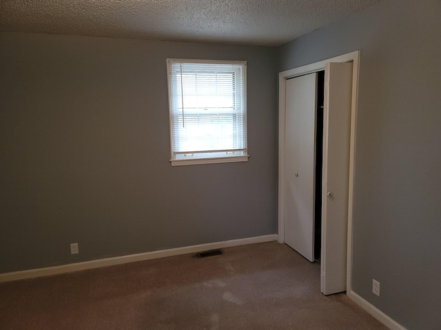 unfurnished bedroom with light carpet, a closet, baseboards, and a textured ceiling