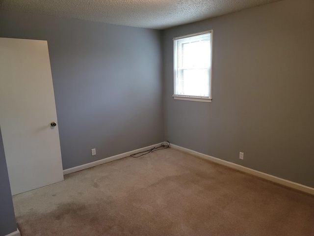 empty room with light carpet, a textured ceiling, and baseboards