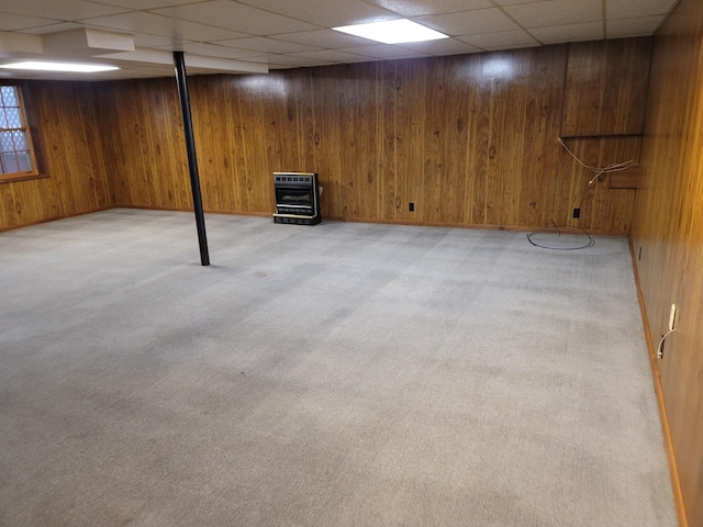 finished basement featuring light carpet, heating unit, wooden walls, and a drop ceiling