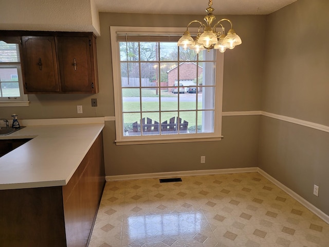 interior space featuring baseboards, visible vents, an inviting chandelier, light countertops, and pendant lighting