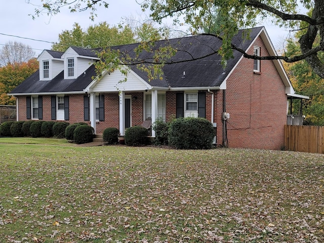 view of front facade with a shingled roof, brick siding, fence, and a front lawn