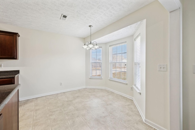 unfurnished dining area featuring a chandelier, visible vents, a textured ceiling, and baseboards