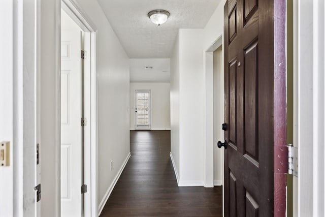 hallway with a textured ceiling, dark wood-type flooring, and baseboards