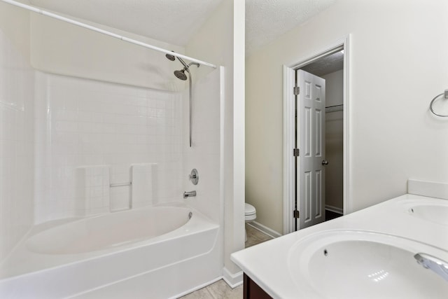 bathroom with double vanity, a textured ceiling, toilet, and a sink