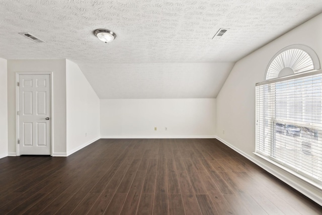 additional living space featuring dark wood finished floors, visible vents, vaulted ceiling, a textured ceiling, and baseboards