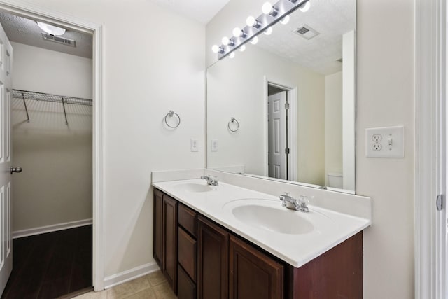 full bath with double vanity, baseboards, a walk in closet, and a sink