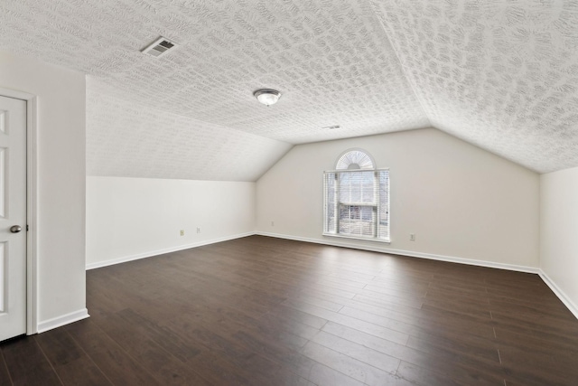 additional living space with a textured ceiling, dark wood-style flooring, visible vents, and baseboards