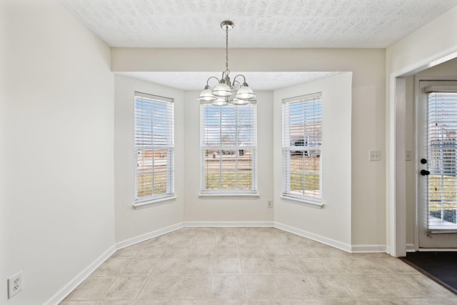 unfurnished dining area featuring a chandelier, a textured ceiling, and baseboards