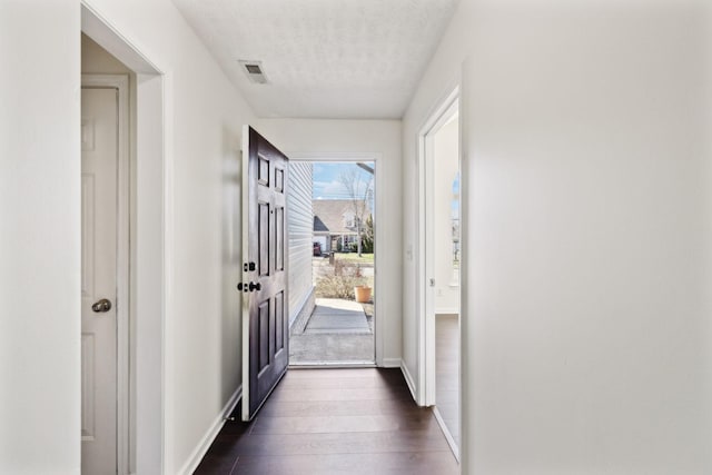 doorway featuring dark wood-style flooring, visible vents, a textured ceiling, and baseboards