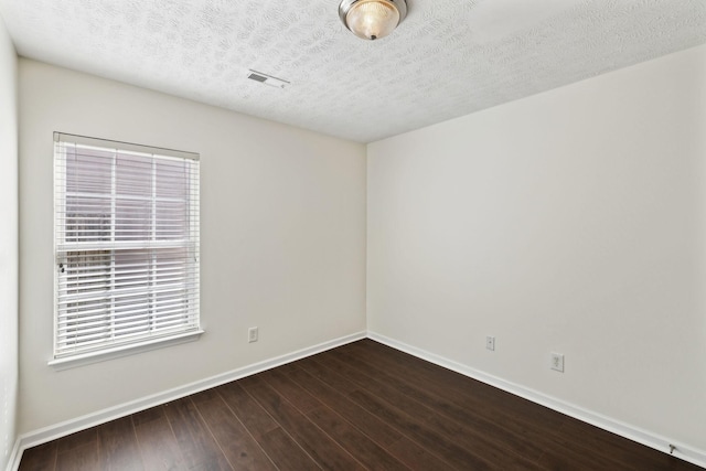 spare room featuring dark wood-style flooring, visible vents, a textured ceiling, and baseboards