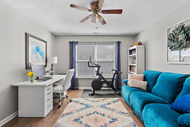 home office featuring a textured ceiling, wood finished floors, a ceiling fan, and baseboards