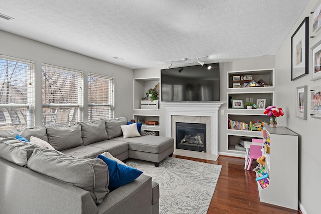 living room with a textured ceiling, built in shelves, a premium fireplace, and wood finished floors