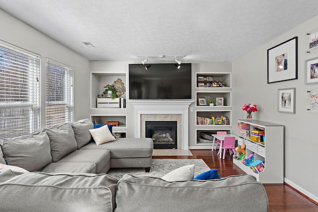 living area with built in features, a fireplace, visible vents, a textured ceiling, and wood finished floors