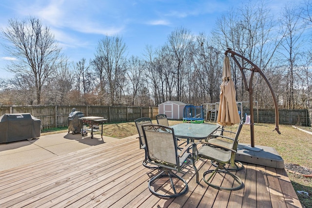 wooden terrace with outdoor dining space, a fenced backyard, an outdoor structure, and a storage unit