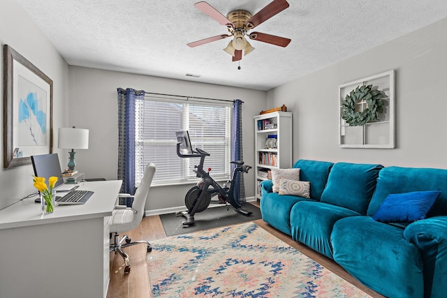 office space with a textured ceiling, wood finished floors, visible vents, baseboards, and a ceiling fan