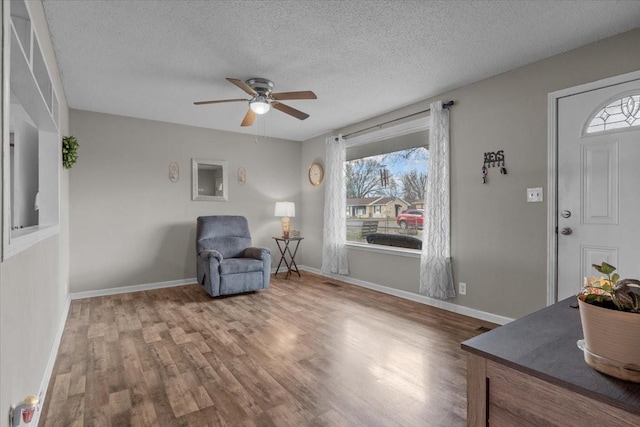 sitting room with ceiling fan, a textured ceiling, baseboards, and wood finished floors