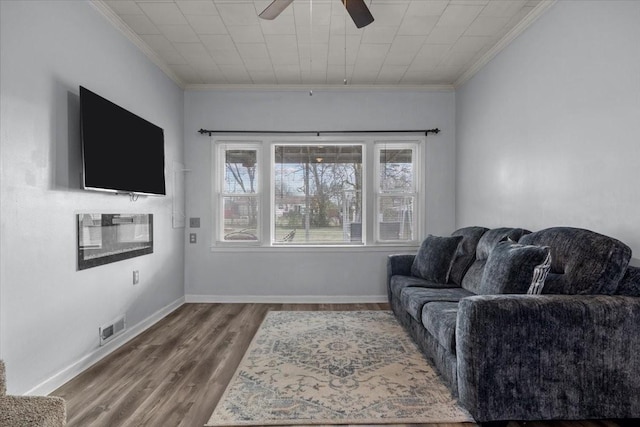 living area with ornamental molding, wood finished floors, visible vents, and baseboards