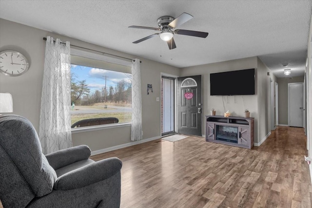 living area with a textured ceiling, ceiling fan, wood finished floors, and baseboards