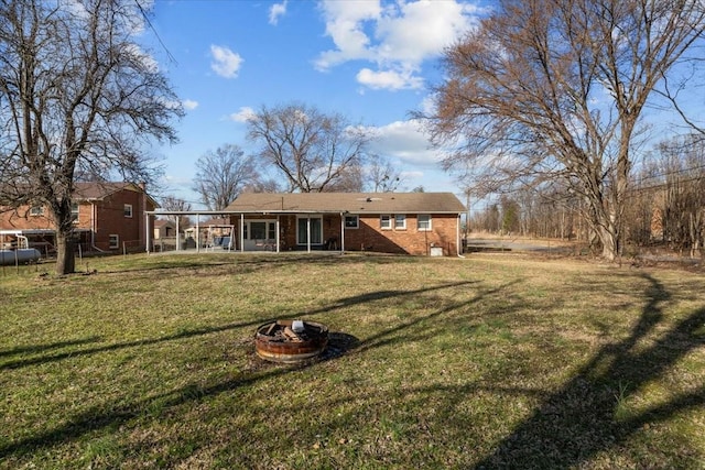 back of property featuring a sunroom, a yard, an outdoor fire pit, and brick siding