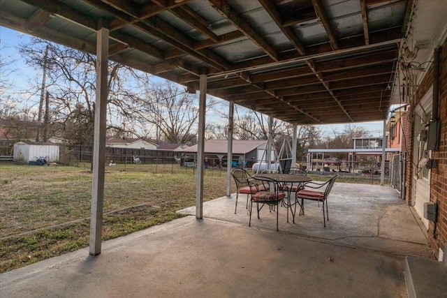 view of patio / terrace featuring an outbuilding, a storage unit, outdoor dining area, and fence