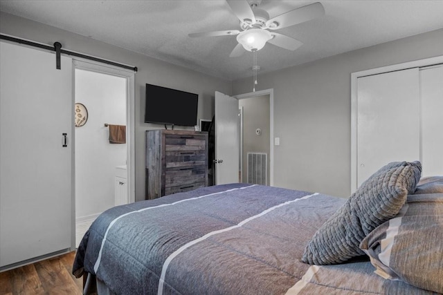 bedroom featuring a barn door, visible vents, a ceiling fan, wood finished floors, and a closet