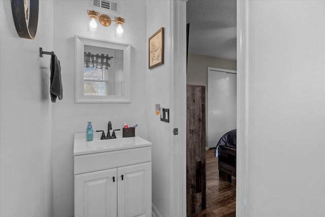 bathroom with a textured ceiling, wood finished floors, vanity, and visible vents