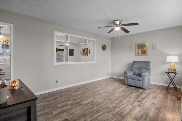 living area featuring a textured ceiling, baseboards, and wood finished floors