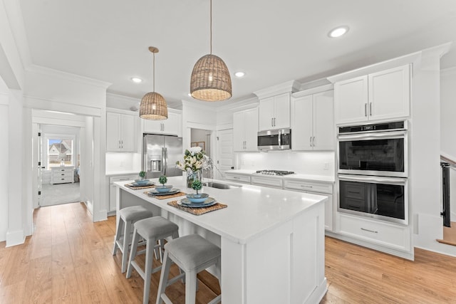 kitchen with light countertops, appliances with stainless steel finishes, a kitchen island with sink, and white cabinetry