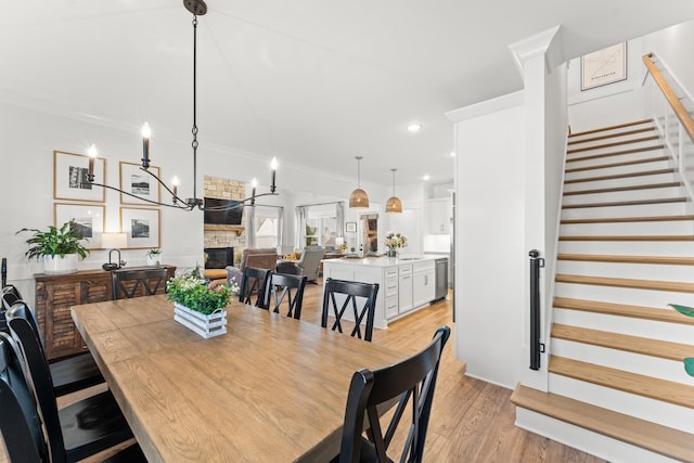 dining space with recessed lighting, a fireplace, light wood-style floors, stairs, and ornamental molding