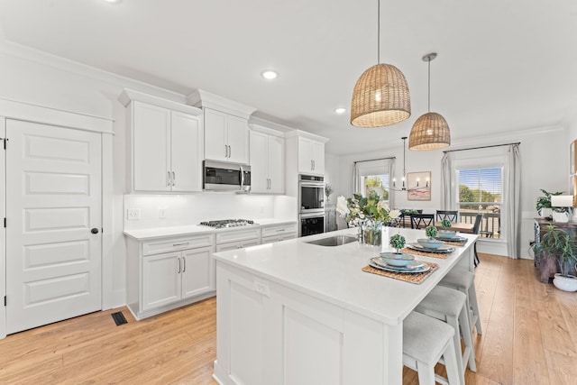 kitchen featuring appliances with stainless steel finishes, light countertops, a kitchen island with sink, and light wood-style flooring