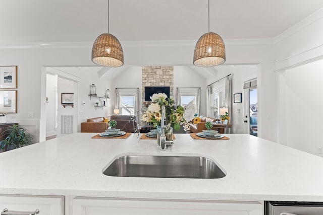 kitchen featuring a sink, white cabinets, open floor plan, hanging light fixtures, and ornamental molding