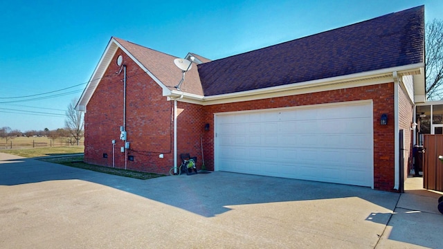 view of side of home with a shingled roof, brick siding, driveway, and an attached garage