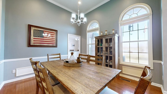 dining space with a notable chandelier, visible vents, hardwood / wood-style floors, ornamental molding, and baseboards