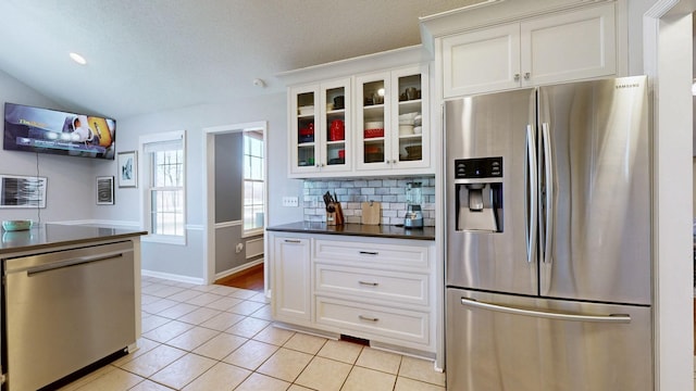 kitchen featuring dark countertops, appliances with stainless steel finishes, glass insert cabinets, backsplash, and light tile patterned flooring