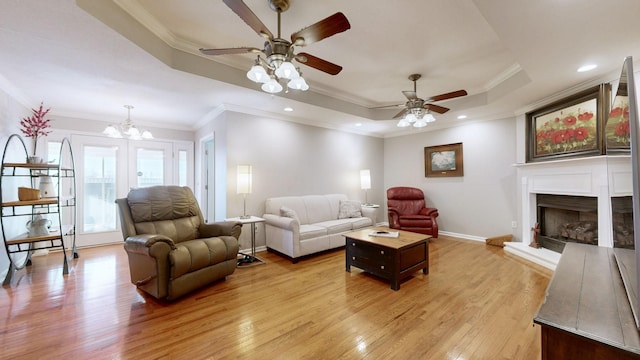 living room with a tray ceiling, crown molding, light wood finished floors, a fireplace with raised hearth, and baseboards