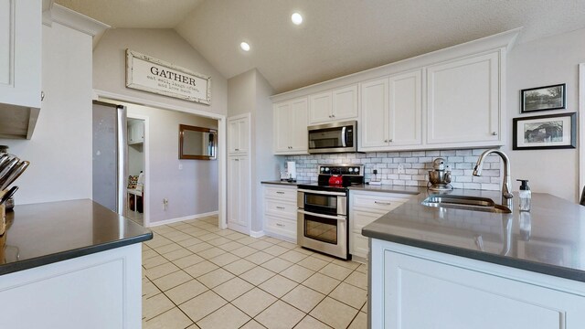 kitchen with light tile patterned flooring, a sink, white cabinets, appliances with stainless steel finishes, and dark countertops