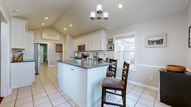 kitchen featuring light tile patterned floors, white cabinets, dark countertops, appliances with stainless steel finishes, and vaulted ceiling