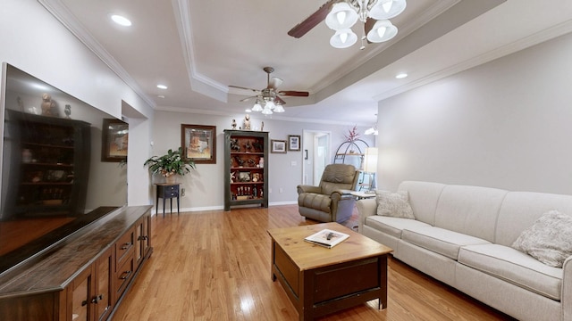 living room featuring light wood finished floors, a tray ceiling, a ceiling fan, and ornamental molding