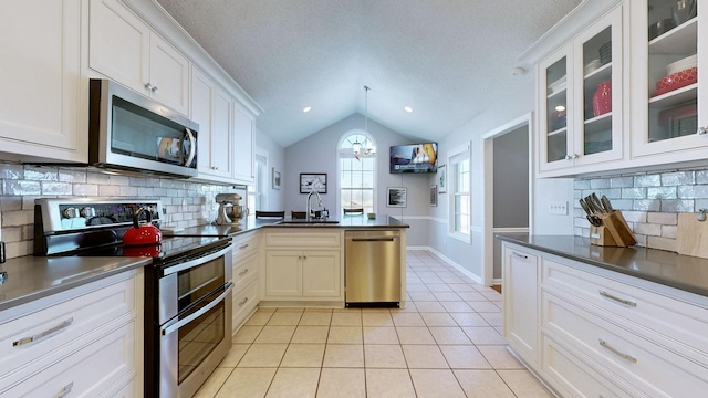 kitchen with stainless steel appliances, lofted ceiling, light tile patterned flooring, a sink, and a peninsula