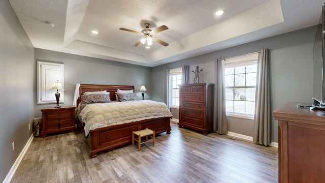 bedroom featuring a tray ceiling, recessed lighting, a textured ceiling, light wood-type flooring, and baseboards