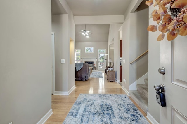 foyer entrance featuring light wood finished floors, baseboards, a fireplace, and stairway