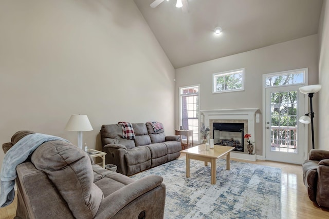 living area featuring a fireplace with raised hearth, high vaulted ceiling, light wood-type flooring, and a ceiling fan