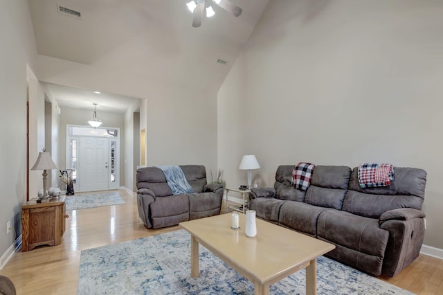 living room with high vaulted ceiling, light wood-type flooring, visible vents, and baseboards