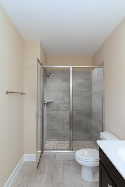 full bathroom featuring vanity, a shower stall, toilet, and baseboards