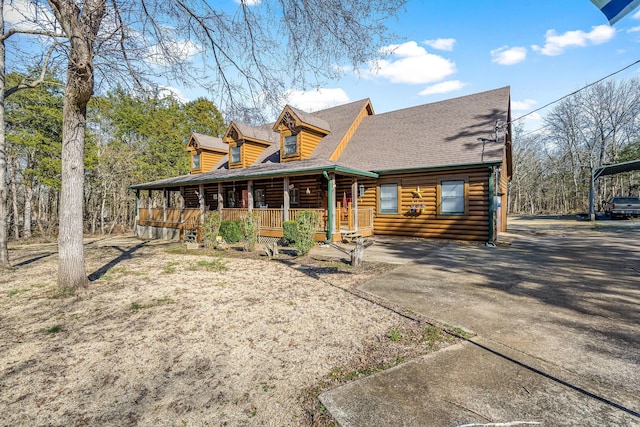 view of front of house featuring covered porch, a shingled roof, driveway, log exterior, and a carport